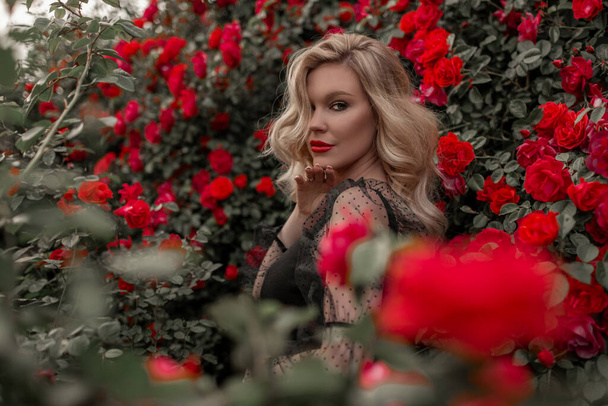 Beautiful blonde woman in garden with red roses. Spring time. - Foto, immagini