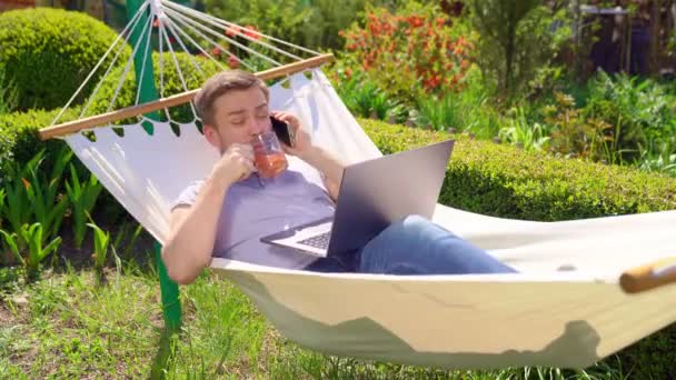 man working on computer while lying in hammock in nature. daughter shakes dad. - Footage, Video