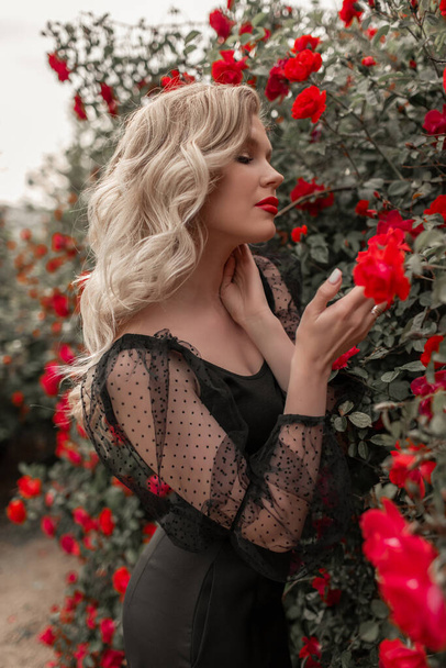 Beautiful blonde woman in garden with red roses. Spring time. - Zdjęcie, obraz
