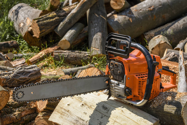 Chainsaw that stands on a heap of firewood in the yard on a background of firewood and trees cut by a chainsaw - Fotoğraf, Görsel