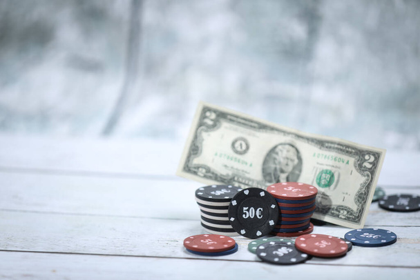 Poker playing chips in focus in front on a wooden table and wooden background Online gambling. Addiction. Falling poker chips and money in blur . Falling money. Losing money - Photo, Image