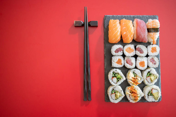 Set of sushi and maki roll.Sushi rolls set with tuna and salmon fish and black chopsticks isolated on red background.Top view.Copy space - Photo, Image