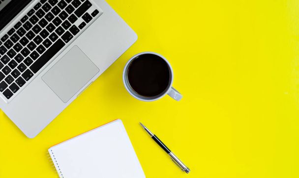 Computador portátil, xícara de café, notebook e caneta em fundo amarelo
 - Foto, Imagem