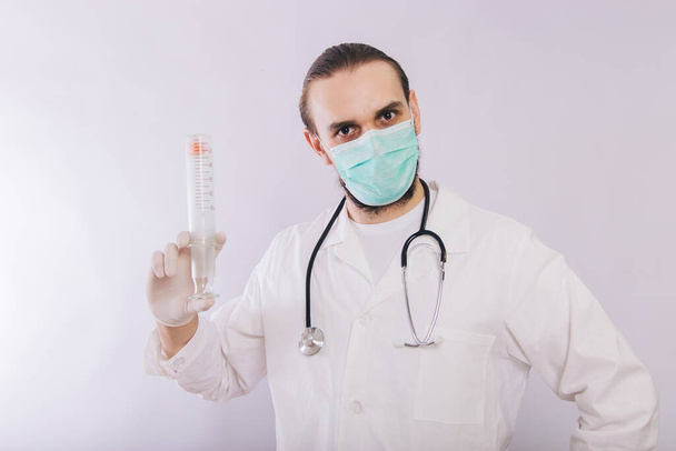 Ein Arzt in weißem Mantel, medizinischer Maske und Handschuhen hält eine große Spritze in der Hand.. - Foto, Bild