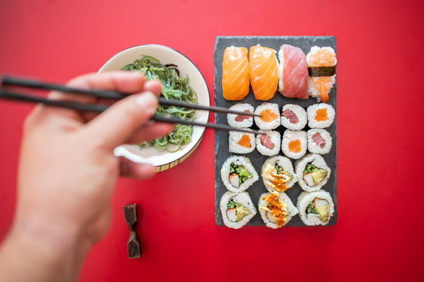 Bovenaanzicht van de hand houden eetstokjes klaar om te eten suhi set en wakame salade. - Foto, afbeelding