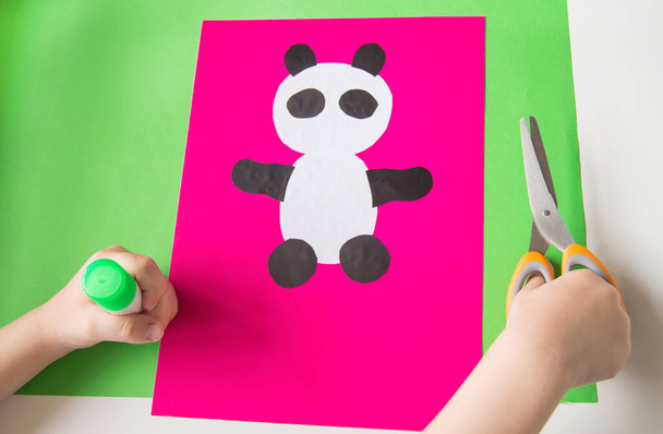 Stap 5. Het kind lijmde de pootjes van de Panda. Het concept van doe-het-zelven en creativiteit van kinderen. Stap-voor-stap instructies: de papieren Panda app. Creatieve activiteiten met een kind tijdens quarantaine. - Foto, afbeelding