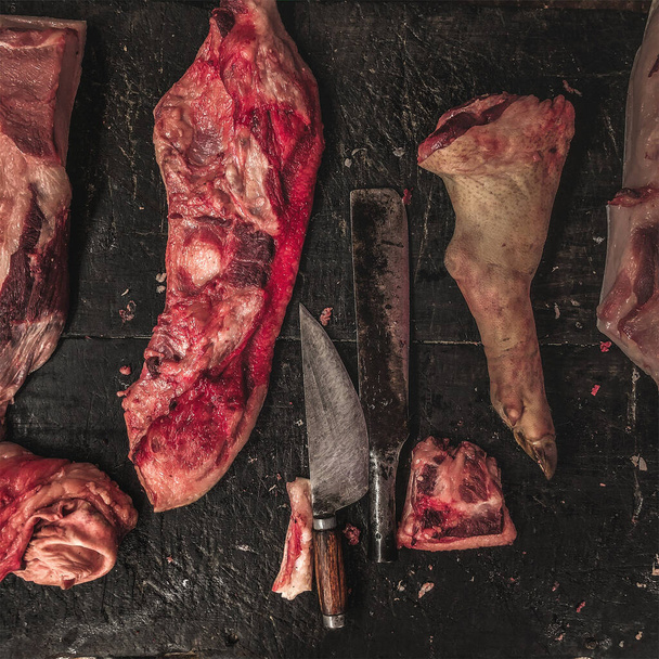 Fleischrohsortiment und Messer auf dem dunklen Holzarbeitstisch des Metzgers. Ansicht von oben. - Foto, Bild