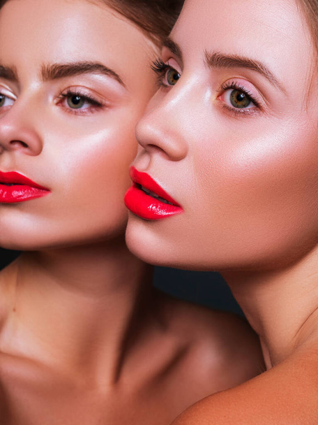 Duas mulheres juntas próximas uma da outra com lábios e olhos vermelhos. Close up conceito de cosméticos de beleza criativa. Pele fresca e sem falhas. Retrato sobre fundo escuro. - Foto, Imagem