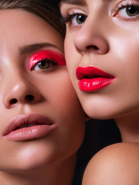 Deux femmes ensemble proches l'une de l'autre avec des lèvres rouges et des yeux. Fermer concept de cosmétiques de beauté créatifs. Peau fraîche sans défaut. Portrat sur fond sombre. - Photo, image