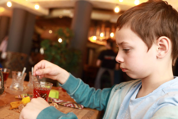 Child stirs sugar in tea in restaurant - Fotó, kép