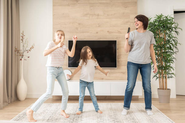 Happy mother and two daughters having fun singing karaoke song in hairbrushes. mother laughing enjoying funny lifestyle activity with teenage girl at home together. - Photo, Image