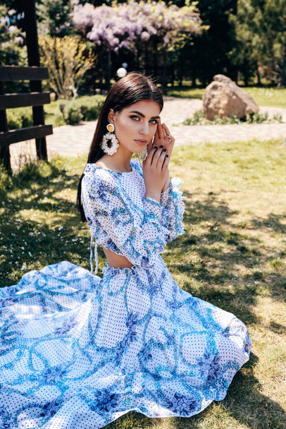 fashion outdoor photo of beautiful sensual woman with dark hair in luxurious dress with accessories posing in summer garden with blooming trees - Foto, Bild