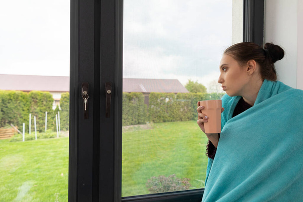 Durante la quarantena, un adolescente guarda fuori dalla finestra con una tazza di tè caldo ed erbe aromatiche
. - Foto, immagini