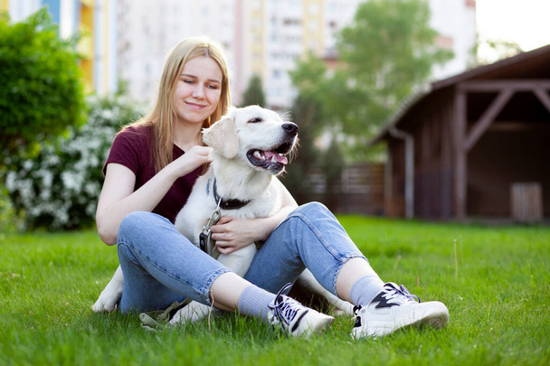 niña con un cachorro de un recuperador se sienta en una hierba verde en la primavera en la calle, una mujer juega con un perro
 - Foto, imagen