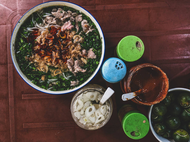 Top kilátás egy hagyományos pho bo egy sötét asztalon. Pho bo vietnami friss rizs tésztaleves marhahússal, gyógynövényekkel és chilivel. Vietnam nemzeti étel - Fotó, kép