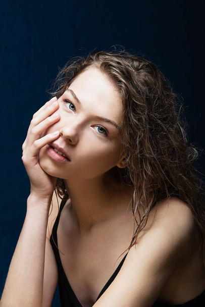 large portrait of a young girl with long curly wet hair, fair skin, holds her hand on her face, looks forward, bare shoulders, smooth skin, blue eyes, attractive young girl - Photo, image