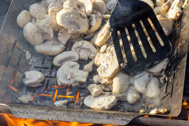 sappige smakelijke champignons koken op grill of BBQ stoom. De kok mengt de champignons met een keukenspatel. Selectieve focus. Voedselachtergrond. Heerlijke gezonde maaltijden voor vegetariërs. - Foto, afbeelding