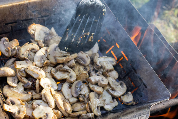 champignons appétissants juteux cuisent sur le gril ou la vapeur de barbecue. Le cuisinier mélange les champignons avec une spatule de cuisine. Concentration sélective. Contexte alimentaire. Délicieux repas sains pour les végétariens
. - Photo, image