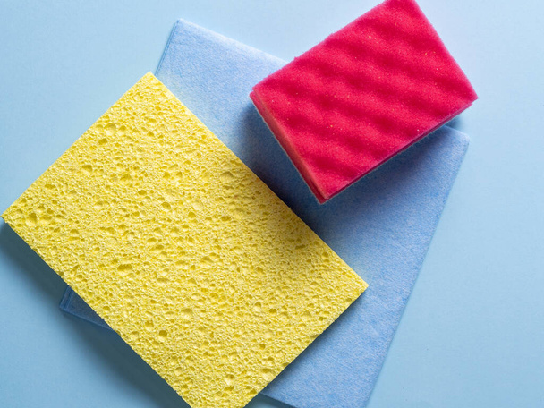 Vista superior de esponjas limpiadoras de diferentes colores y tamaños dispuestas sobre un fondo azul - Foto, Imagen