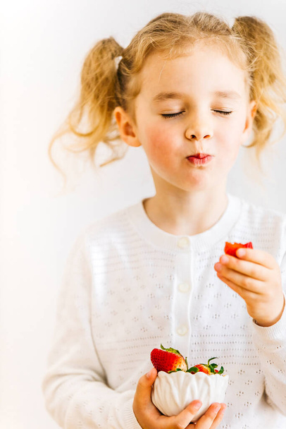 Aardbei. Beetje blij peuter meisje houden en eten biologische aardbeien op witte achtergrond met kopieerruimte. Kind eet seizoensgebonden zelfgekweekte aardbeien.Levensstijl van een gelukkige kindertijd.Gelukkige Vaderdag - Foto, afbeelding