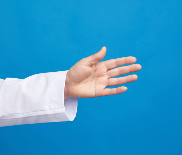 medic in a white coat pulls his hand for a handshake on a blue background, close up - Valokuva, kuva