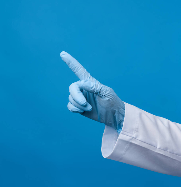 medic woman in white coat, wearing in blue sterile gloves, showing hand gesture indicating the subject, blue background - Photo, Image