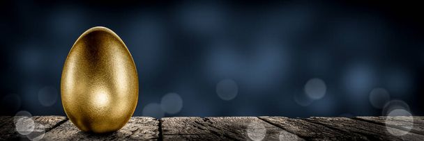 Złote gniazdo na drewnianym stole z niebieskim tłem - koncepcja planu inwestycyjnego / emerytalnego - Zdjęcie, obraz