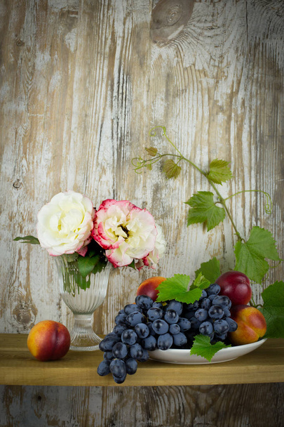 Vintage still Life with roses, grapes and peaches on an old wooden background. Vertically, copy space - Photo, Image