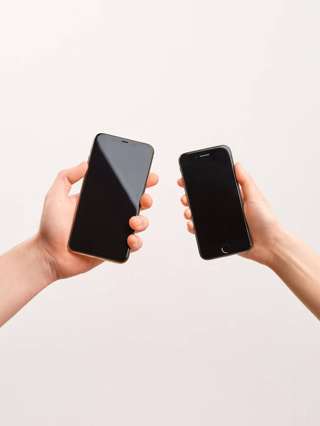 Smartphones of different generations with empty screens in the hands of a man and a woman close-up on a white background - Fotó, kép