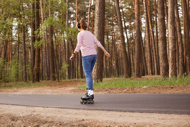 Outdoor image of energetic sleder young woman having training, being active, rollerblading alone, having rest, relaxing, enjoying weekends, being on road, listening to music. Lifestyle concept. - Photo, image