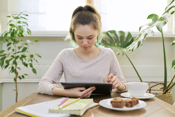 Teenager girl studying at home, student sitting at table using digital tablet - Фото, изображение