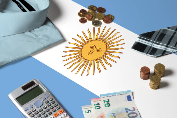 Argentina flag on minimal money concept table. Coins and financial objects on flag surface. National economy theme. - 写真・画像