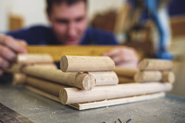 Egy férfi ács egy fával dolgozik egy asztalosműhelyben. Csinálok egy modellt egy faházról. - Fotó, kép