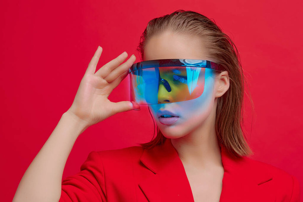 A cool stylish girl with a fashionable hairstyle and stylish glasses with a large glass poses on a bright red background - Valokuva, kuva