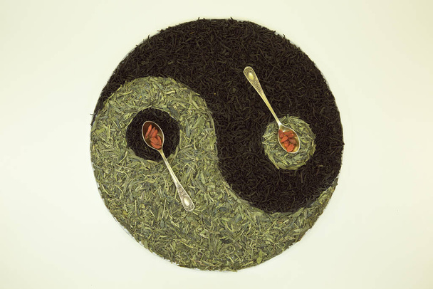 Sign Yin Yang with tea. Used Chinese black tea, green Lundzin, goji and two spoons. Healthy eating concept. - Photo, Image