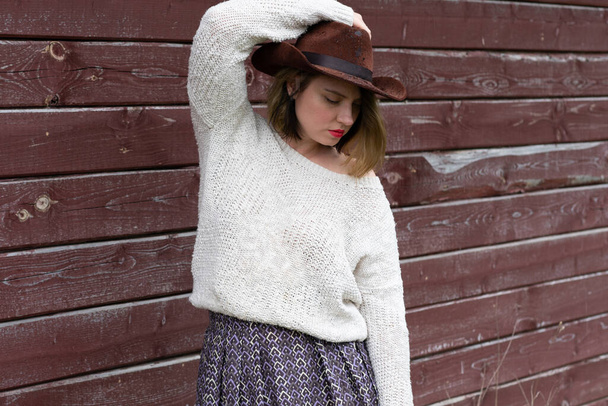 νεαρή όμορφη κοπέλα στέκεται κοντά σε ένα ξύλινο αχυρώνα σε ένα λευκό πουλόβερ - Φωτογραφία, εικόνα