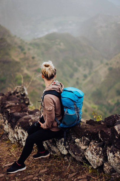 Female hiker with blue backpack staying on the stony cobbled trekking trail leading down to the valley between barren mountain peak on Santo Antao island, Cabo Verde - Fotoğraf, Görsel