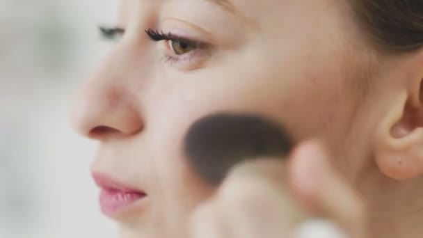 Beauty woman applying makeup. Beautiful girl looking in the mirror and applying cosmetic with a big brush. Girl gets blush on the cheekbones. Powder, rouge. - Footage, Video