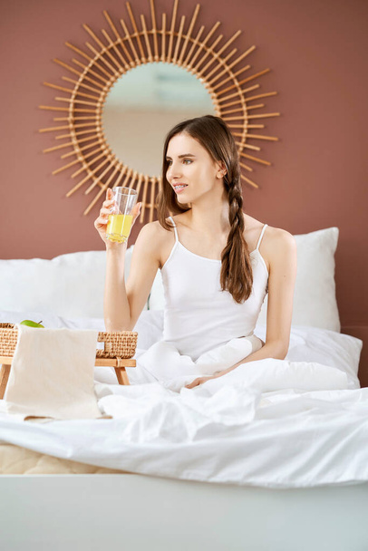 Smiling girl with braces sits on bed and holds glass with juice - Zdjęcie, obraz