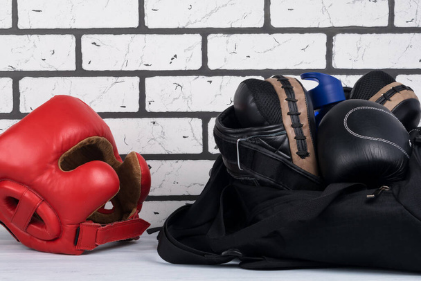 черный спортивная сумка с вещами для тренировок и красный защитный боксерский шлем на фоне кирпичной стены
 - Фото, изображение