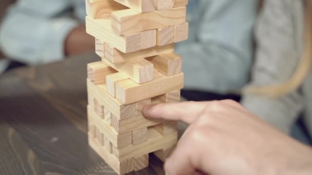 Tower of wooden blocks. Close-up hands of friends playing block removal game on a table. - Video