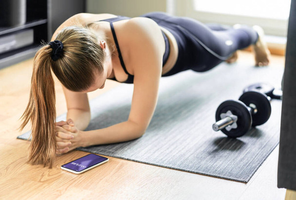 Home exercise and bodyweight training, plank. Fit woman taking time with sport tracker app in phone. Workout routine in living room gym. Yoga, pilates or aerobics. Functional core strength motivation. - Photo, Image