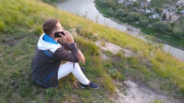 Facet siedzi na wzgórzu i gada przez telefon. - Materiał filmowy, wideo