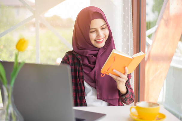 Donna musulmana con hijab sta lavorando con il computer portatile in caffetteria - Foto, immagini
