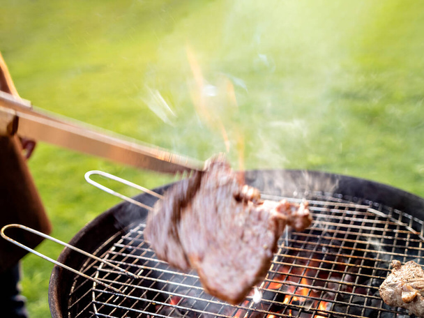 Gedeocaliseerde scène van een man grillen vlees buiten. - Foto, afbeelding