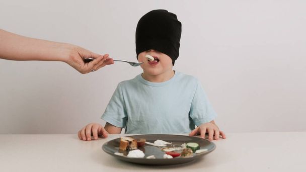 Un niño con una máscara negra intenta adivinar una variedad de alimentos
 - Foto, Imagen