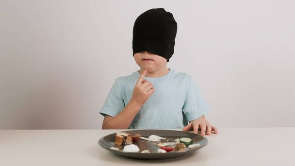 A boy in a black mask tries and guesses a variety of foods - Photo, Image