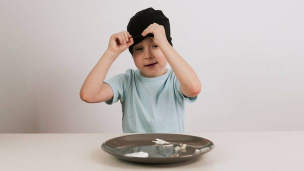 Een jongen met een zwart masker probeert en raadt een verscheidenheid aan voedsel en geeft duimen op - Foto, afbeelding