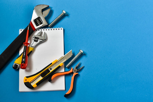 Construction tools for repair on a blue background. Place for text. The concept of construction, repair. Hammer, notebook for writing, screw, pliers. - Foto, imagen