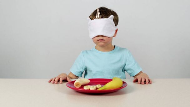 Little boy in a mask tries and guesses banan - Photo, Image